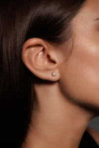 Close-up dell’orecchio della modella con Orecchini Punto Luce in Argento 925 placcato oro giallo e brillante bianco, un gioiello classico e luminoso.